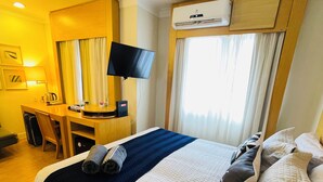 Ein Hotelzimmer mit Bett, Schreibtisch, Stuhl, Fernseher und Klimaanlage.