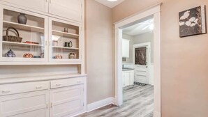 A hallway with a white cabinet displaying various items, a wooden floor, and a doorway leading to another room. - Avalon Nest - Both Units (Memphis)
