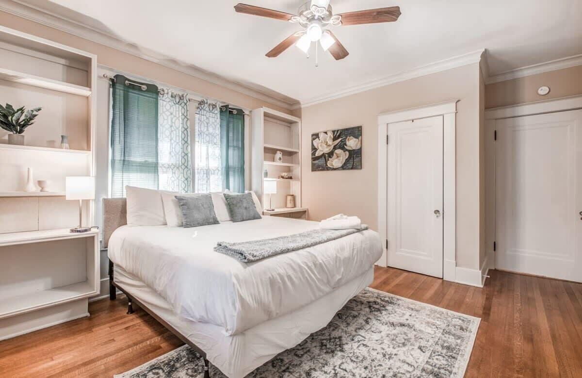 A bedroom with a large bed, a ceiling fan, built-in shelving, and a door.