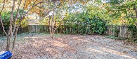 A backyard with a paved patio, trees with autumn foliage, and a wooden fence.