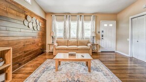Ett vardagsrum med en väggpanel av trä, en beige soffa, ett soffbord och en mönstrad matta.