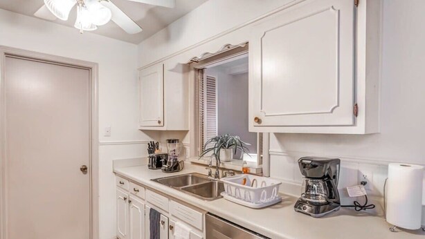 A kitchen with white cabinets, a dishwasher, a coffee maker, and a sink. - Pinecrest Cottage (Memphis)