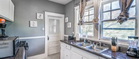 A kitchen with white cabinets, a granite countertop, a double sink, and a window with curtains.
