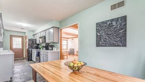 Una cucina con un tavolo di legno, una ciotola di frutta e un elemento decorativo in metallo appeso al muro.