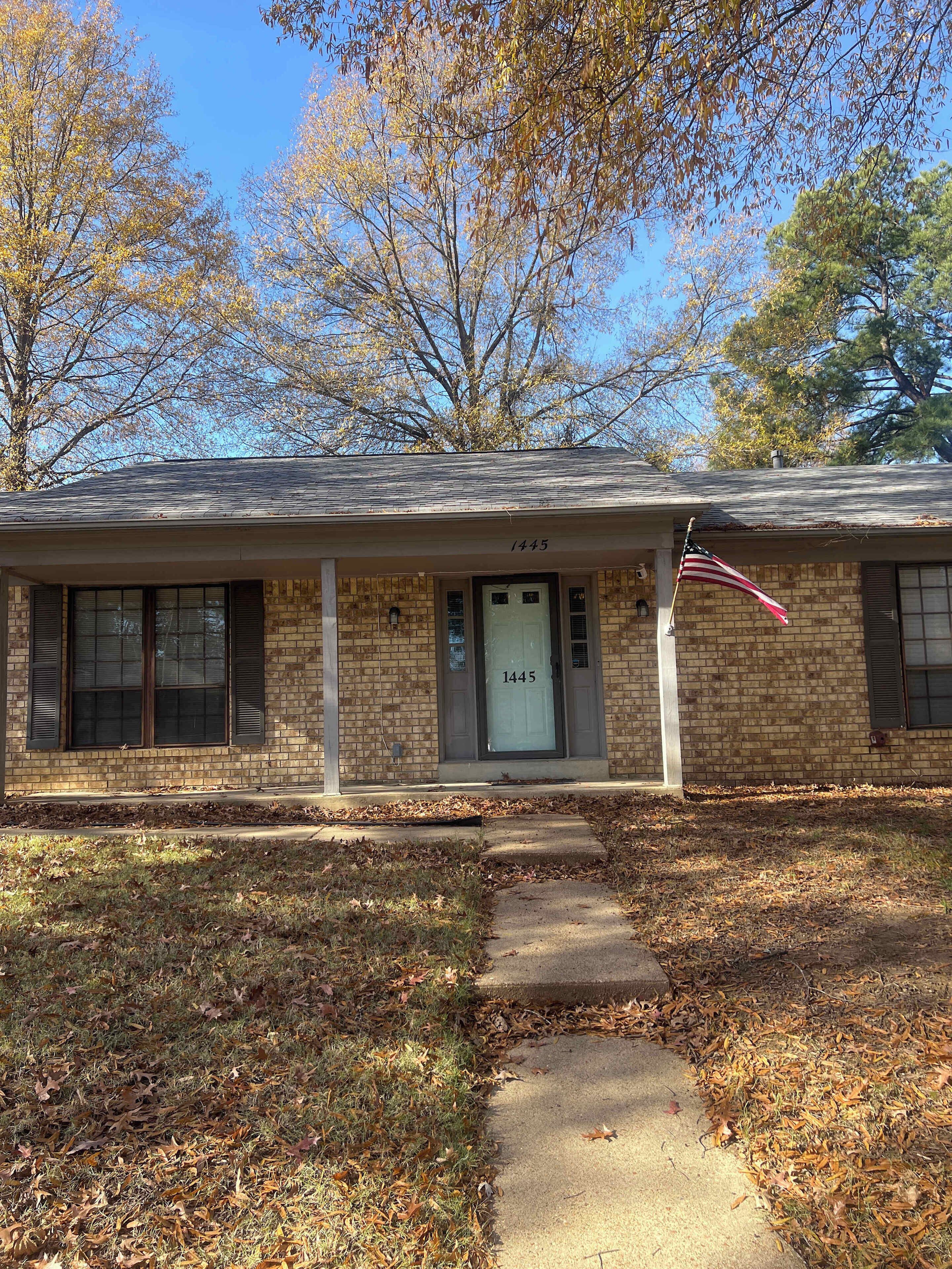 A two-story brick house with a front porch, a visible mailbox, and an American flag.