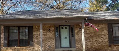 A two-story brick house with a front porch, a visible mailbox, and an American flag.