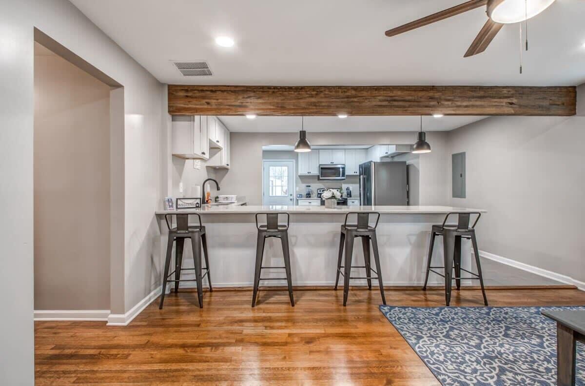 A modern kitchen with a wooden ceiling, white cabinets, and a bar area with stools.