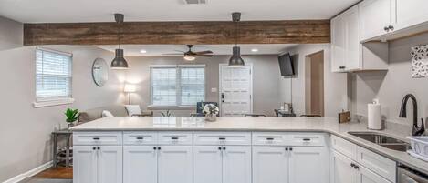 A modern kitchen with white cabinetry, a large island, pendant lighting, and a ceiling fan.