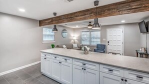 Een moderne keuken met witte kasten, een groot eiland, hangende lampen en een plafond met houten balken.