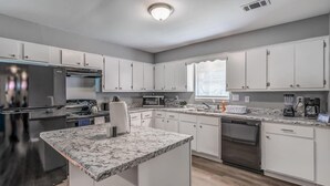 A modern kitchen with white cabinets, granite countertops, stainless steel appliances, and a window providing natural light.