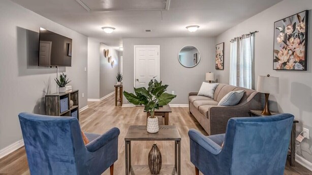 A living room with a grey sofa, two blue armchairs, a coffee table, and a TV mounted on the wall.
