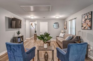 A living room with a grey sofa, two blue armchairs, a coffee table, and a TV mounted on the wall. - Schoolfield Collective (Memphis)