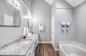 A bathroom with a large mirror, two sinks, a bathtub, and wooden flooring.