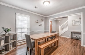 A dining area with a wooden table and bench, a staircase, and a small kitchen area.