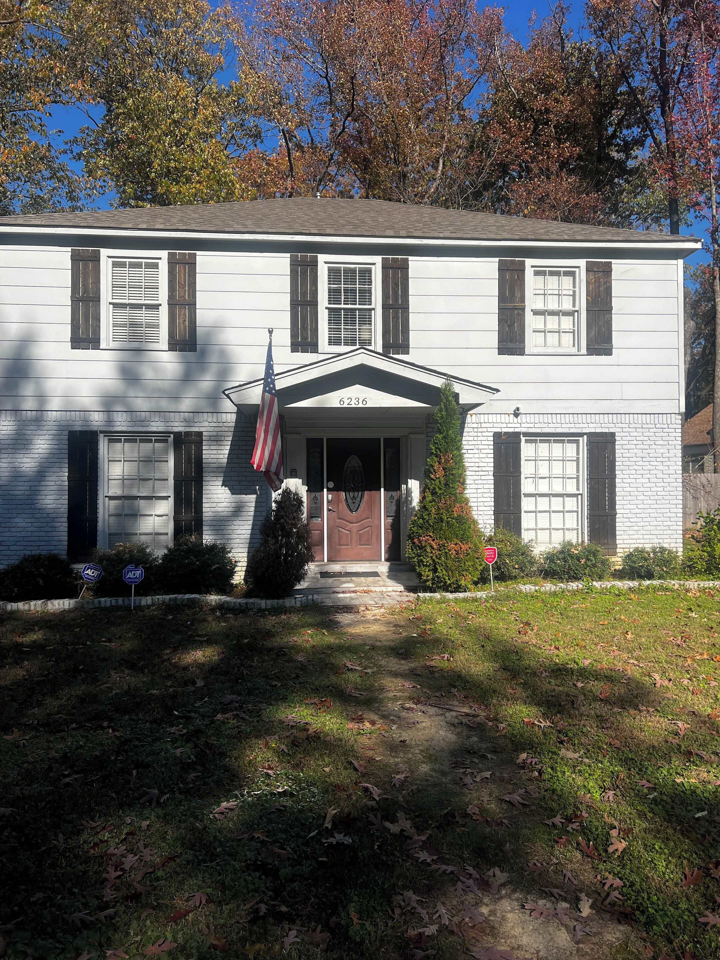 A two-story white building with a central entrance, a small porch, and a flag.