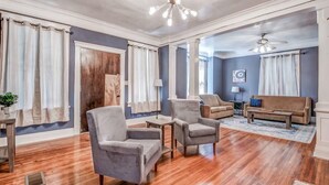 A spacious living room with hardwood flooring, a chandelier, and a ceiling fan. - Glenview Guesthouse (Memphis)