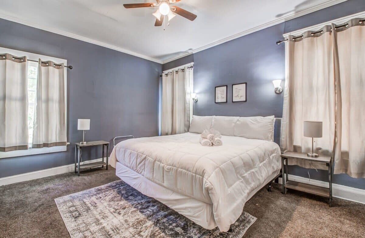 A bedroom with a large bed, two bedside tables, a ceiling fan, and a window with curtains.