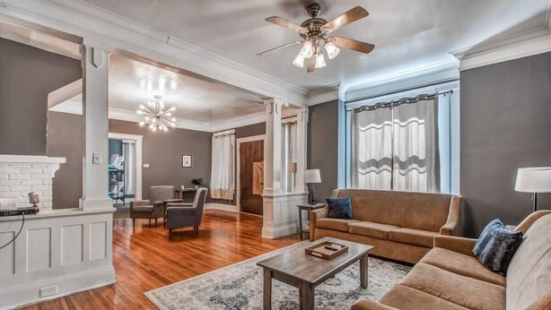 A spacious living room with a fireplace, a ceiling fan, and a large window with curtains. - Glenview Guesthouse (Memphis)