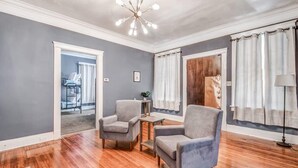 A living room with a wooden floor, two grey armchairs, a small table, and a ceiling light fixture. - Glenview Guesthouse (Memphis)