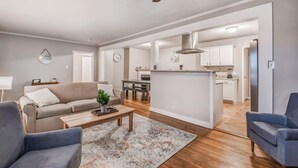 A modern living room with a sofa, coffee table, and a rug. There is a kitchen area visible through an open doorway. - Flamingo Hideaway (Memphis)