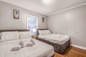 Habitación de hotel con dos camas, una ventana con persianas y una mesita de noche con lámpara.