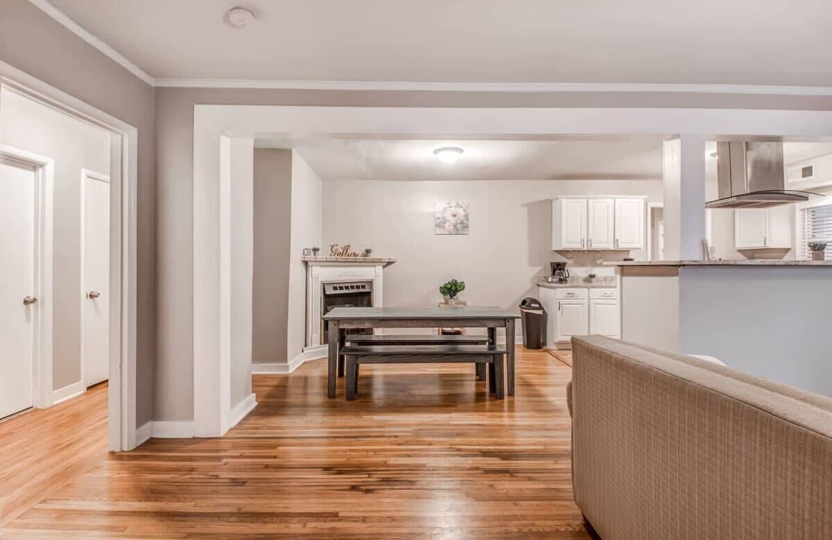 A modern kitchen with white cabinets, a central island, and a dining area with a wooden table and bench.