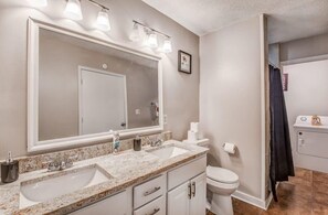 Un baño con un espejo grande, dos lavamanos, inodoro y zona de ducha.