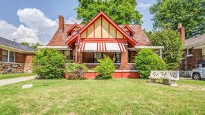 A two-story house with a red and white striped awning, brick exterior, and a front yard with a bench and a small tree. - Garland Haven Hideaway Unit A (Memphis)