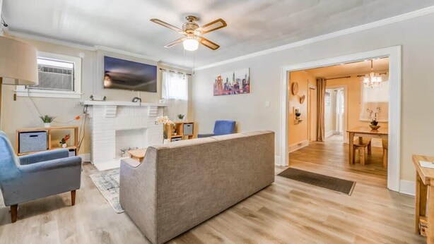 A modern living room with a sofa, a blue armchair, a fireplace, a ceiling fan, and a dining area visible through an open doorway. - Garland Haven Hideaway Unit A (Memphis)