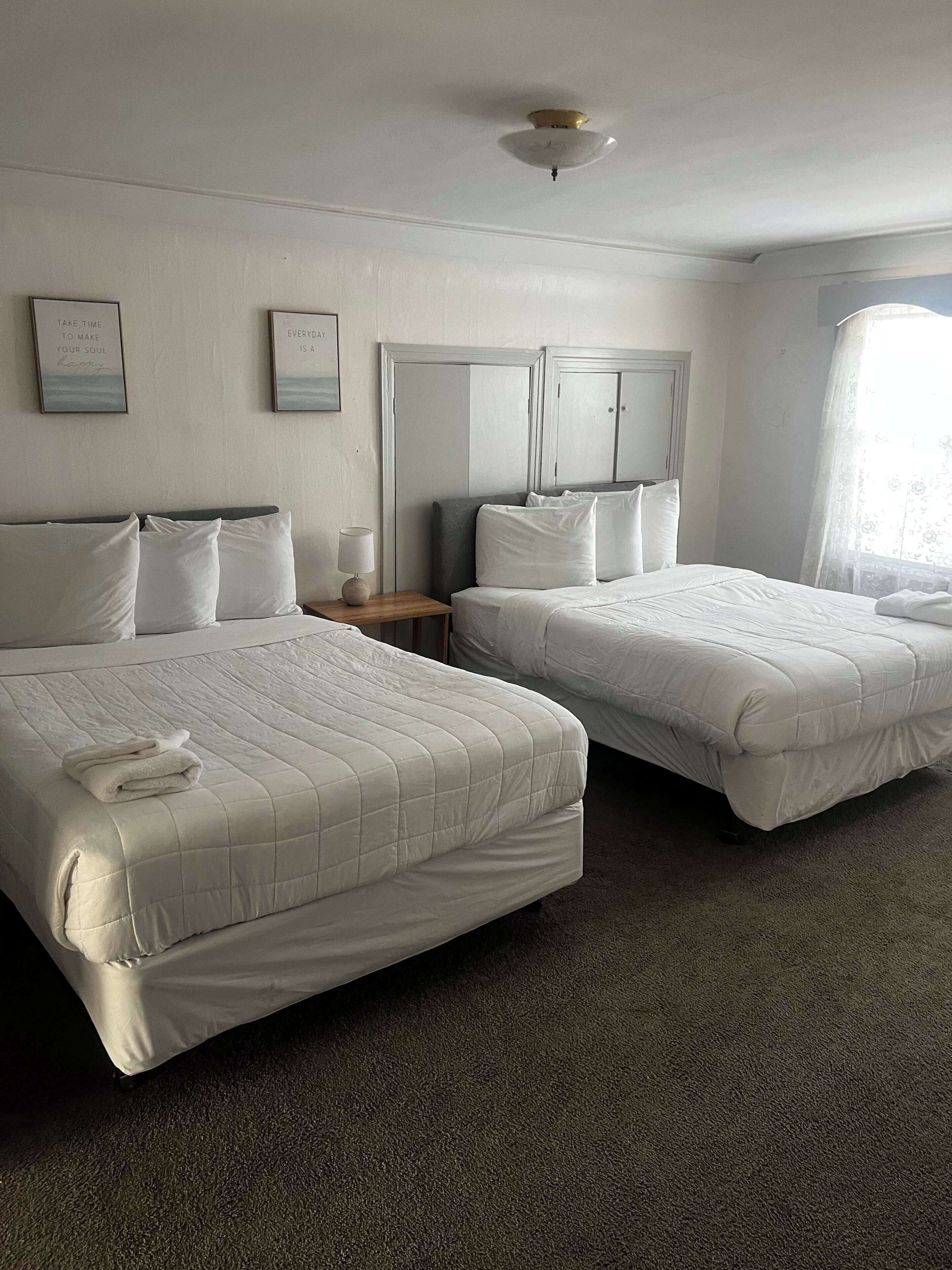 A hotel room with two beds, a nightstand, a lamp, and a ceiling fan.