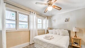 A bedroom with a bed, a ceiling fan, a nightstand with a lamp, and a window with curtains. - Garland Haven Hideaway Unit A (Memphis)