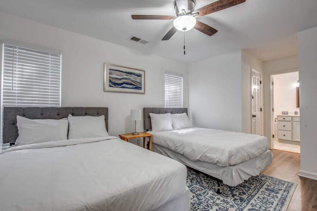 A bedroom with two beds, a ceiling fan, a painting, and a door leading to a bathroom.