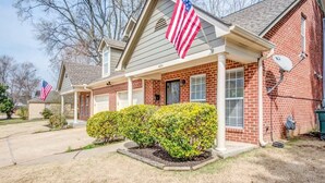 A two-story brick house with a front porch, American flags, and a satellite dish. - High Point Nest Both Units (Memphis)