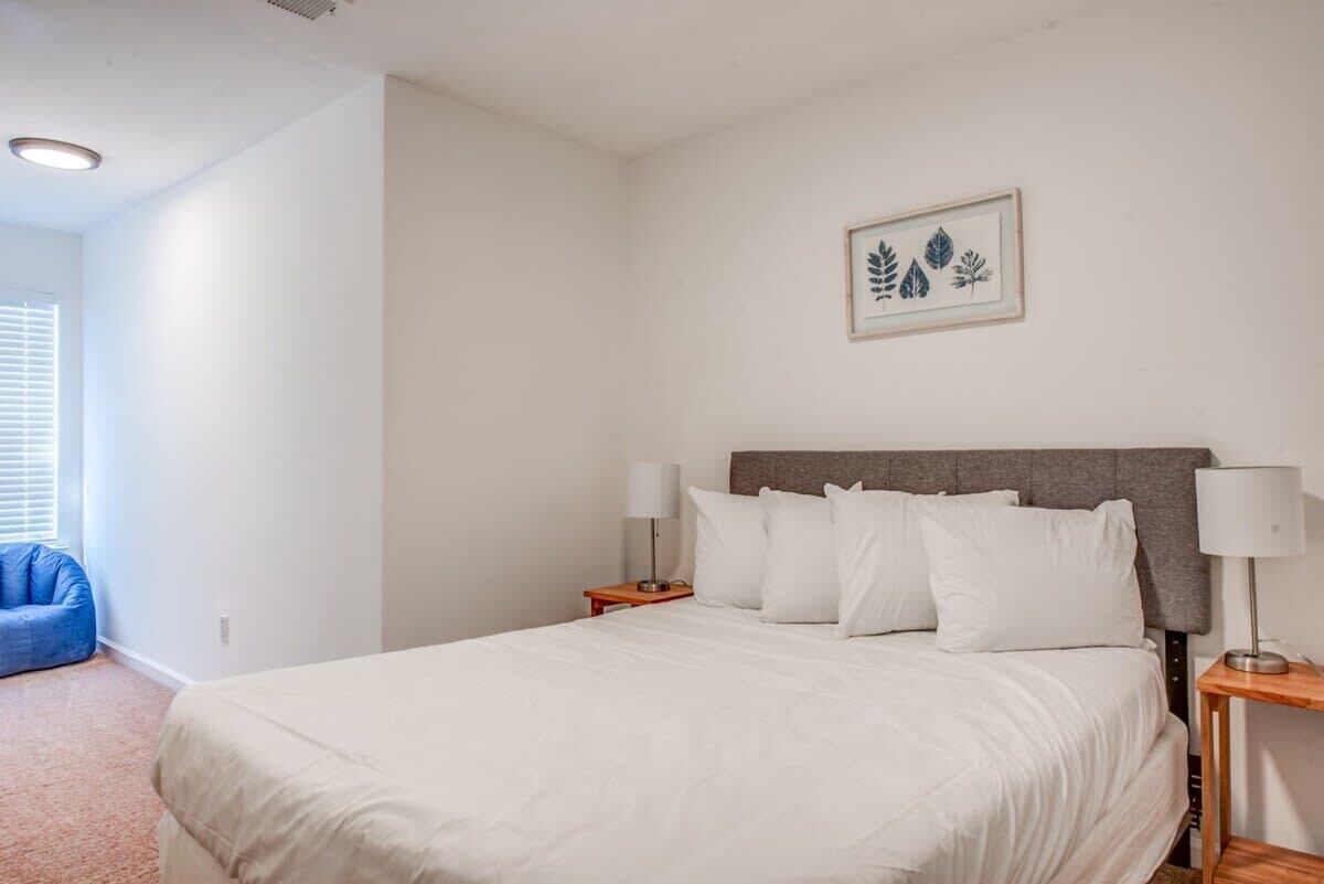 Une chambre à coucher avec un lit, deux tables de chevet, une petite table, une chaise bleue et une œuvre d’art représentant une feuille, encadrée et accrochée au mur.