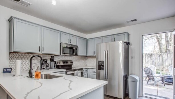 A modern kitchen with white cabinets, stainless steel appliances, and a large island with a sink. - High Point Nest Both Units (Memphis)