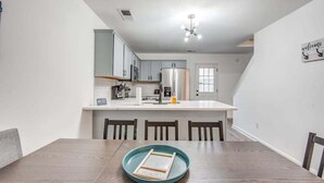 A modern kitchen with white cabinets, a central island, and a dining area with a wooden table and chairs. - High Point Nest Both Units (Memphis)