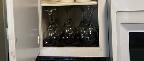 A kitchen cabinet with two shelves, one holding white cups and the other holding wine glasses.