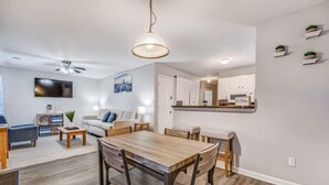 A modern living room with a wooden dining table, a sofa, and a TV mounted on the wall. - Cedar Ave Escape (Memphis)