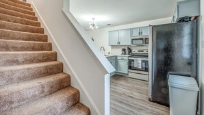 Un escalier mène à une cuisine dotée de meubles de couleur bleu clair, d’un réfrigérateur en acier inoxydable et d’un four à micro-ondes.