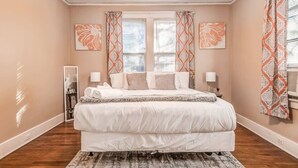 Ein Schlafzimmer mit einem großen Bett, zwei Nachttischen, einem Deckenventilator und einem Fenster mit gemusterten Vorhängen.