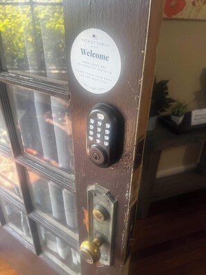 A door with a Yale lock, a welcome sign, and a phone number for door code activation. - Avalon Nest Downstairs (Memphis)