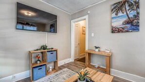 A modern living room with a wooden coffee table, a TV mounted on the wall, and a painting of a beach scene.