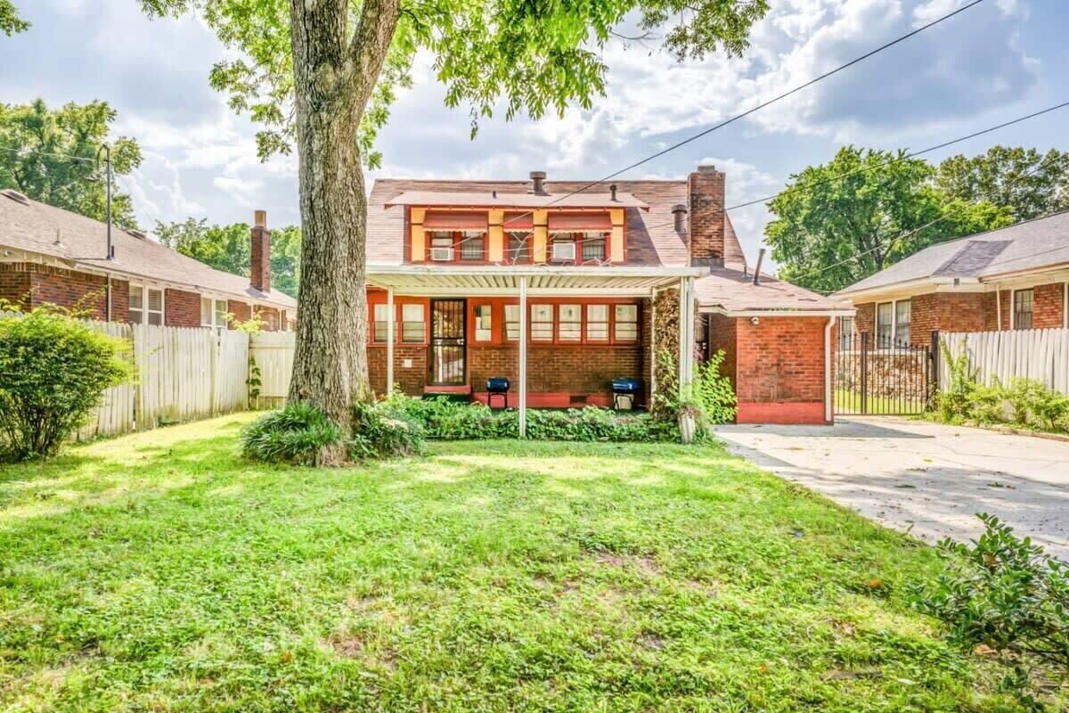 A two-story house with a covered porch, a brick chimney, and a fenced yard.