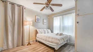 A bedroom with a bed, a ceiling fan, a floor lamp, and a window with curtains.