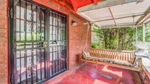 A covered porch with a swing seat, a black gate, and a brick wall.
