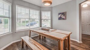 Un'area pranzo con tavolo e panche in legno, ampie finestre con tende, una lampada a sospensione e una porta sulla destra.