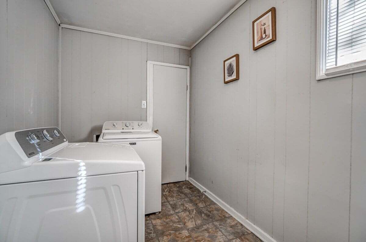 Een wasserette met een voorlader wasmachine en droger, een deur en twee foto's in lijsten aan de muur.