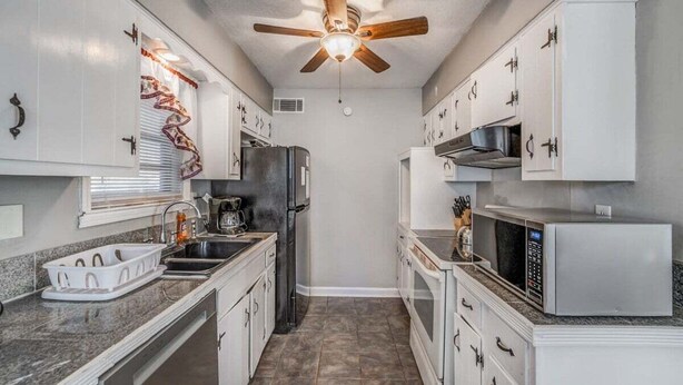 A compact kitchen with white cabinets, a ceiling fan, a refrigerator, a microwave, and a sink.