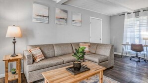 A living room with a grey sofa, a wooden coffee table, and a lamp. There are three paintings on the wall and a door in the background. - Yale Gather Hideaway (Memphis)