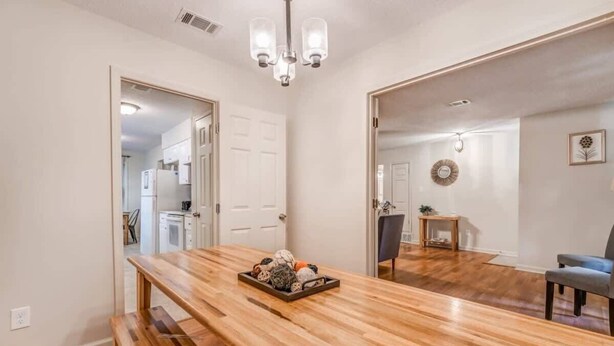 Uma ampla área de jantar com mesa de madeira e bancos, um candelabro e vista para a cozinha e a sala de estar.